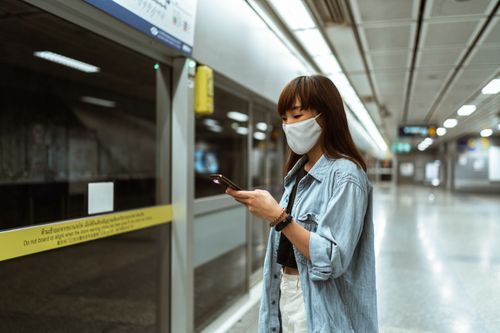 Free Asian woman wearing a face mask, using her smartphone while waiting at an empty metro station. Stock Photo