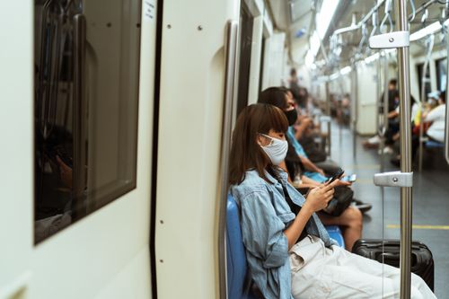 Free Asian woman wearing a face mask, texting on a subway train during pandemic travel. Stock Photo