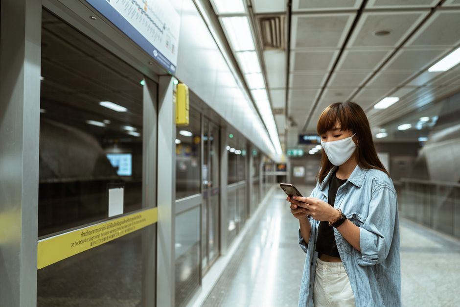 Asian woman in denim jacket using smartphone at subway station.