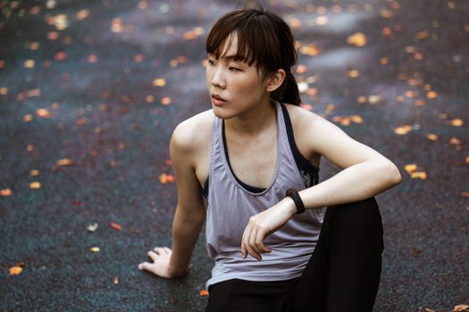 一名女子穿着运动服，若有所思地坐在绿树成荫的小路上，显得十分宁静