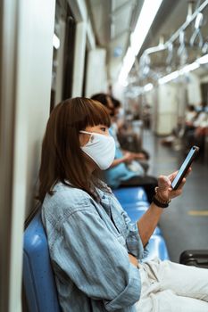 大流行期间，亚洲妇女在公共交通工具上戴着口罩使用智能手机