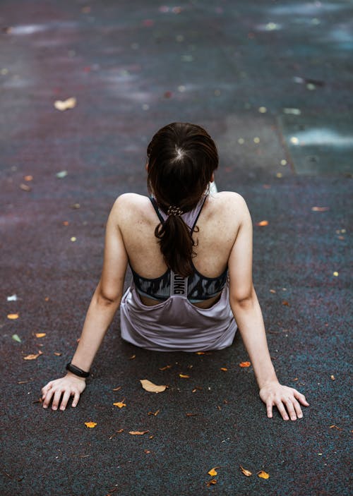 Unrecognizable female in sports clothes sitting on asphalt road