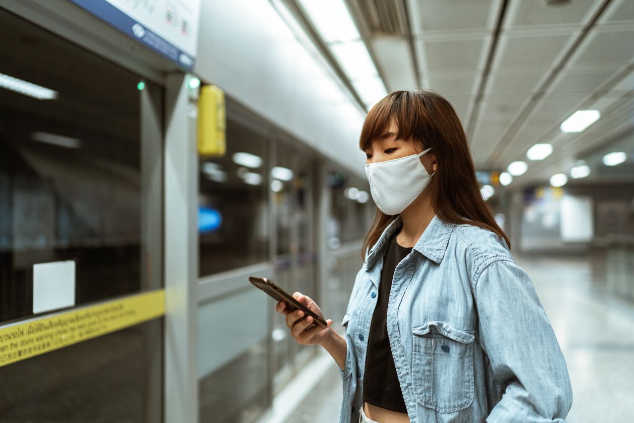 asian woman wearing a face mask using smartphone standing in a subway