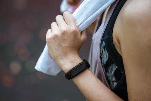 Crop unrecognizable sportswoman in smart watch using towel after workout