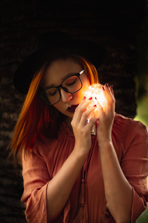 Photo of a Woman with Red Hair Holding a Light Bulb