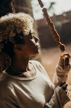 Portrait of a young woman with curly hair holding a skewer outdoors, showcasing a serene and contemplative mood.