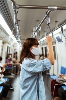 Asian woman wearing a denim jacket and face mask on a subway train, observing COVID-19 precautions.