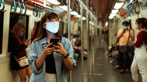 Free Asian woman wearing a face mask using a smartphone on a subway train during COVID-19 pandemic. Stock Photo