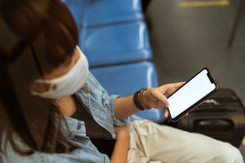 Free Woman Wearing a Face Mask and Holding a Smartphone Stock Photo