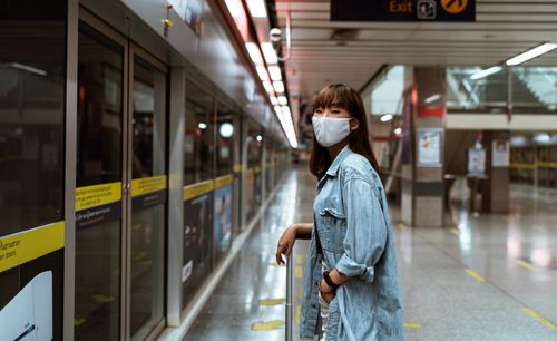 Free An adult woman in a denim jacket and face mask waits at an indoor subway station. Stock Photo