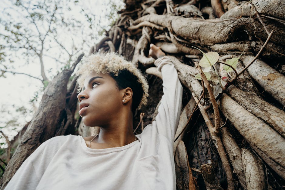 Young woman with curly hair in a natural jungle environment, gazing thoughtfully.