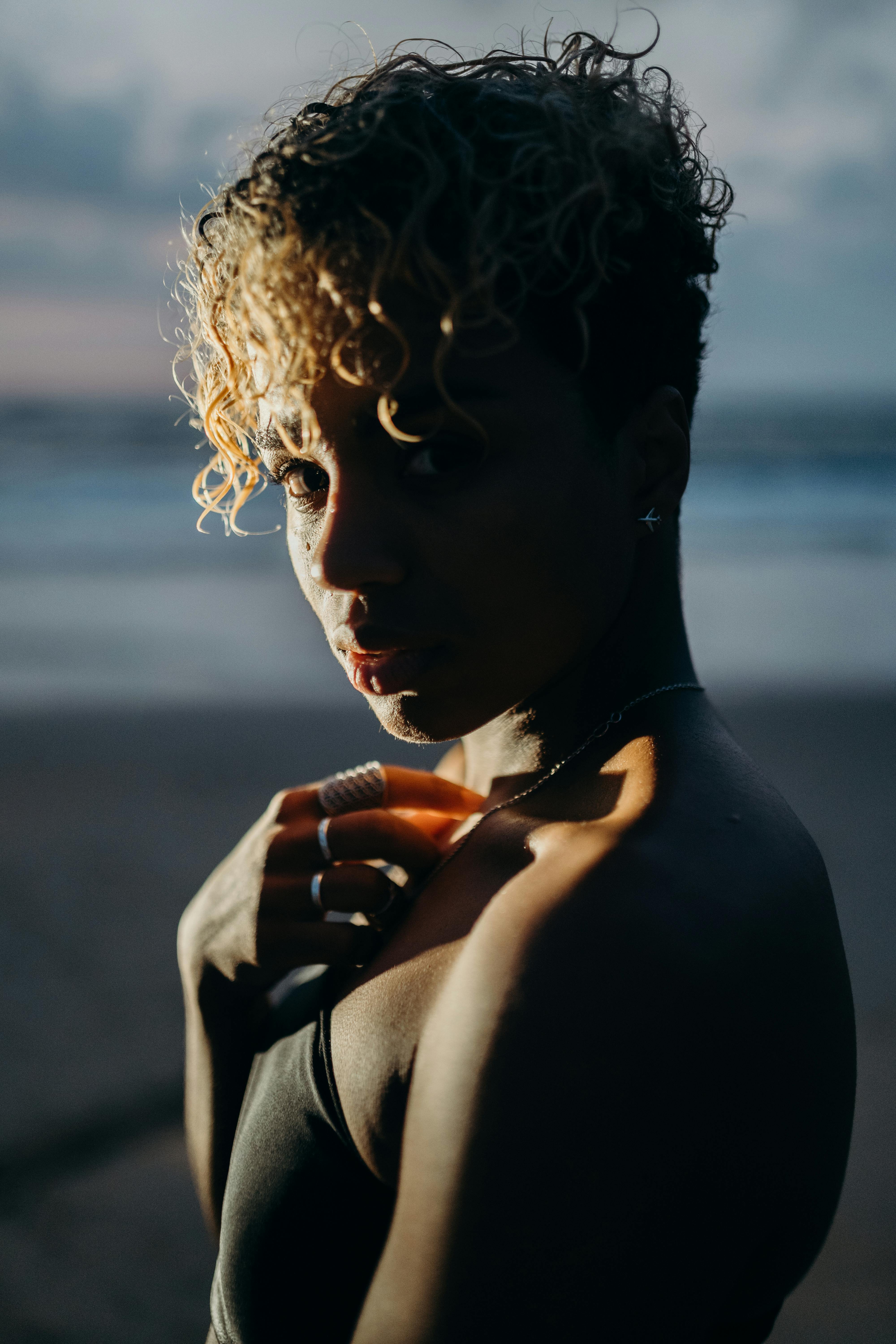 Portrait of a woman with curly hair framed by twilight beach setting, showcasing natural beauty.