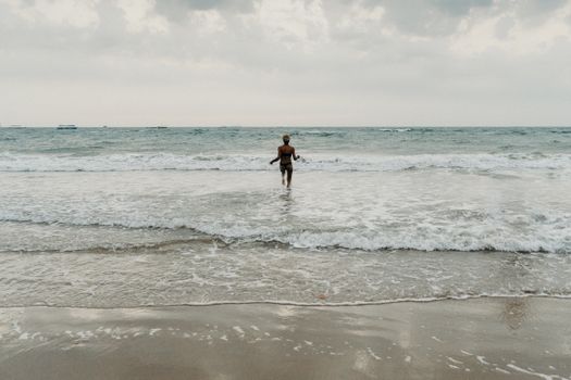 在一个宁静的海滩日子里，一名卷发的年轻女子涉水走向大海