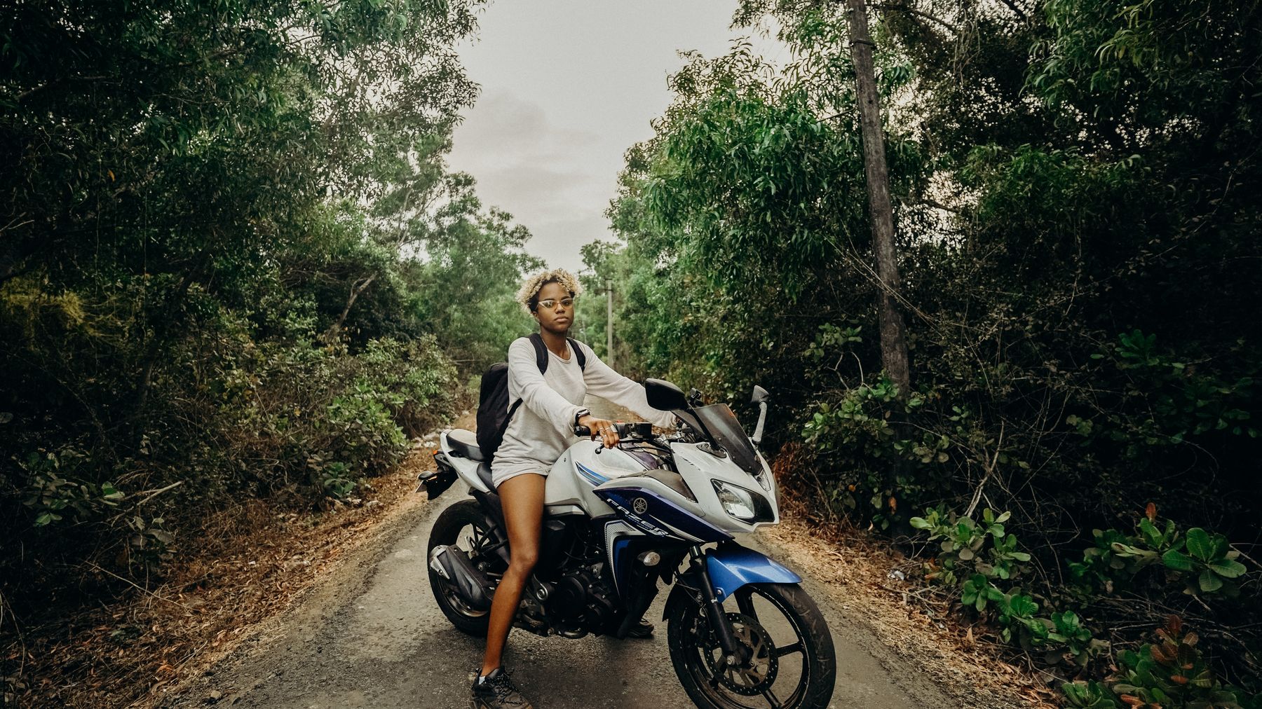 A young woman rides a motorcycle through a lush jungle road, exuding adventure and freedom.