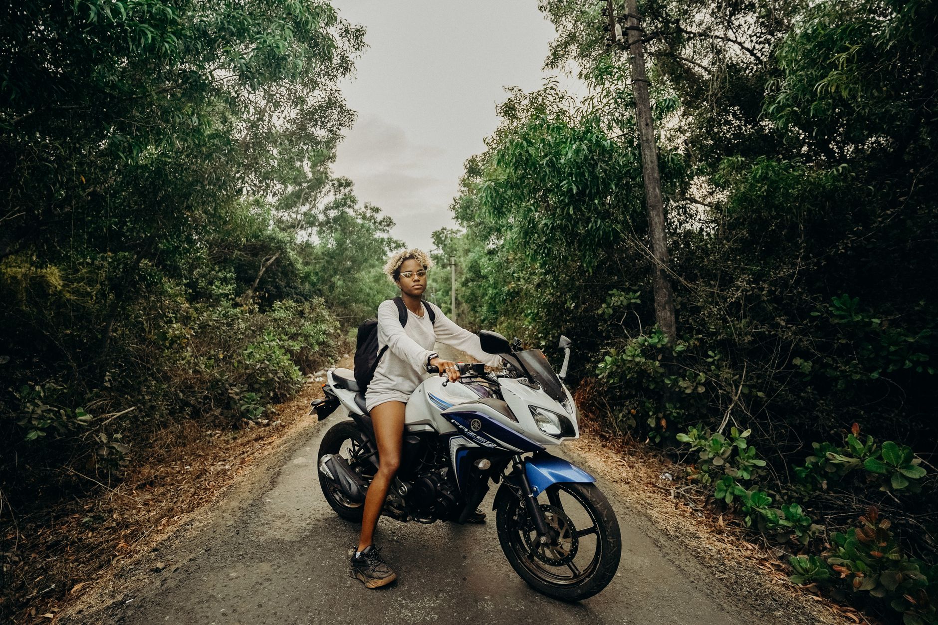 A young woman rides a motorcycle through a lush jungle road, exuding adventure and freedom.