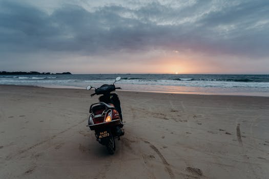 A motorcycle is parked on a tranquil Goa beach as the sun sets over the ocean. Perfect for travel inspiration.