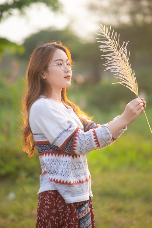 Positive Asian woman with cereal ear on green grassland