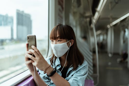 A young woman wearing a face mask on a subway train, using her smartphone.