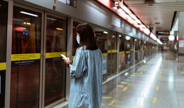 在地铁站等候时，一名戴口罩的女子正在使用智能手机