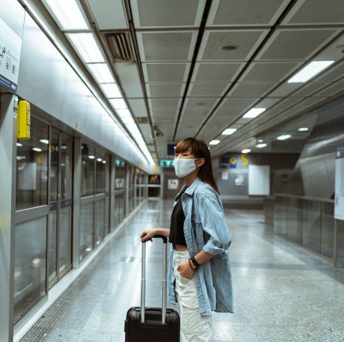 Free A woman wearing a face mask stands with luggage in a subway terminal, ready for travel. Stock Photo