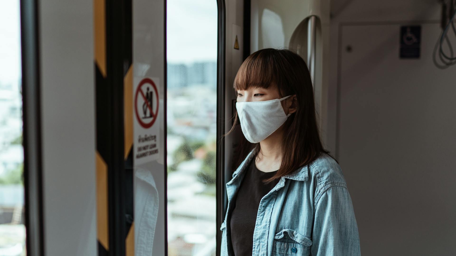 Asian woman with mask on subway, reflecting pandemic travel impact.