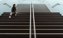 一个女人坐在现代室内的楼梯上，若有所思，传达出一种沉思的心情