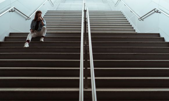 一个女人坐在现代室内的楼梯上，若有所思，传达出一种沉思的心情