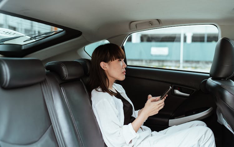 Calm Woman In White Casual Wear Using Smartphone In Car