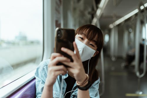 Frau, Die Eine Gesichtsmaske Trägt Und Ein Smartphone Hält
