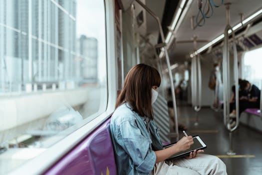 Asian woman taking notes on a tablet while commuting on a subway during pandemic.