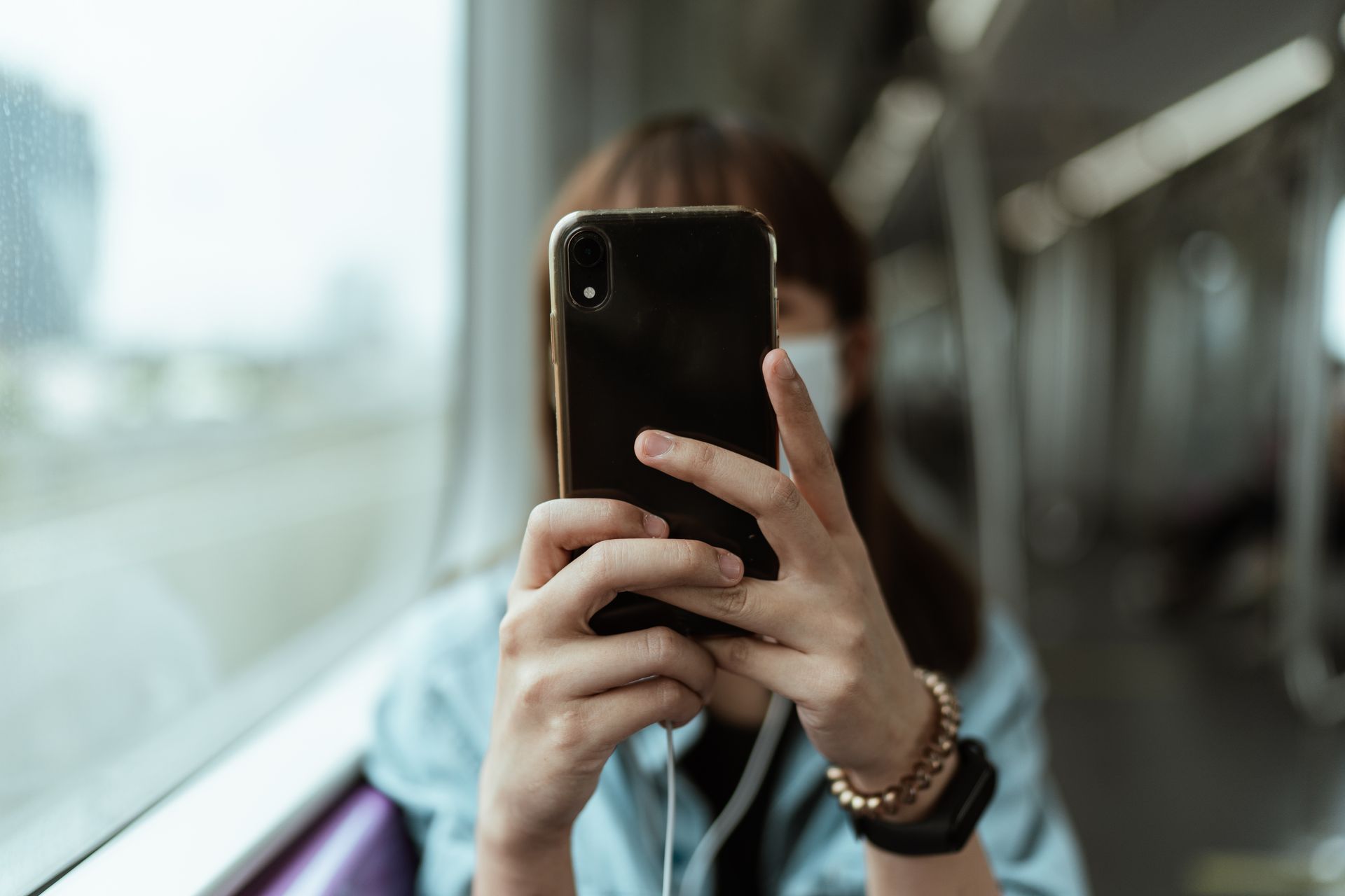Person wearing a mask using smartphone on a subway train.