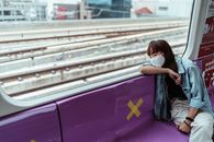 一名戴着口罩的妇女躺在地铁列车座位上，可以看到外面的铁轨