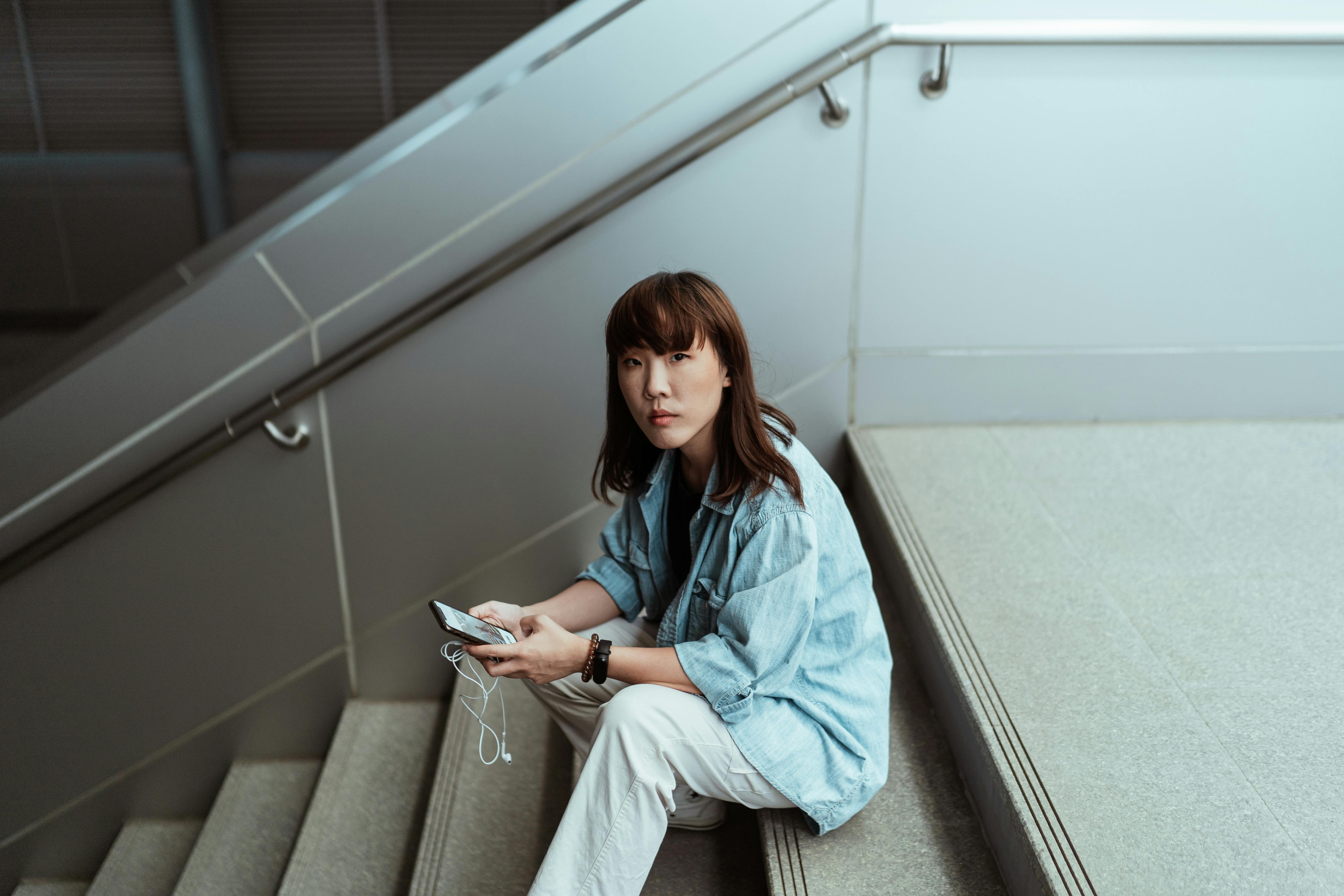 asian woman surfing internet on smartphone while sitting on stairs