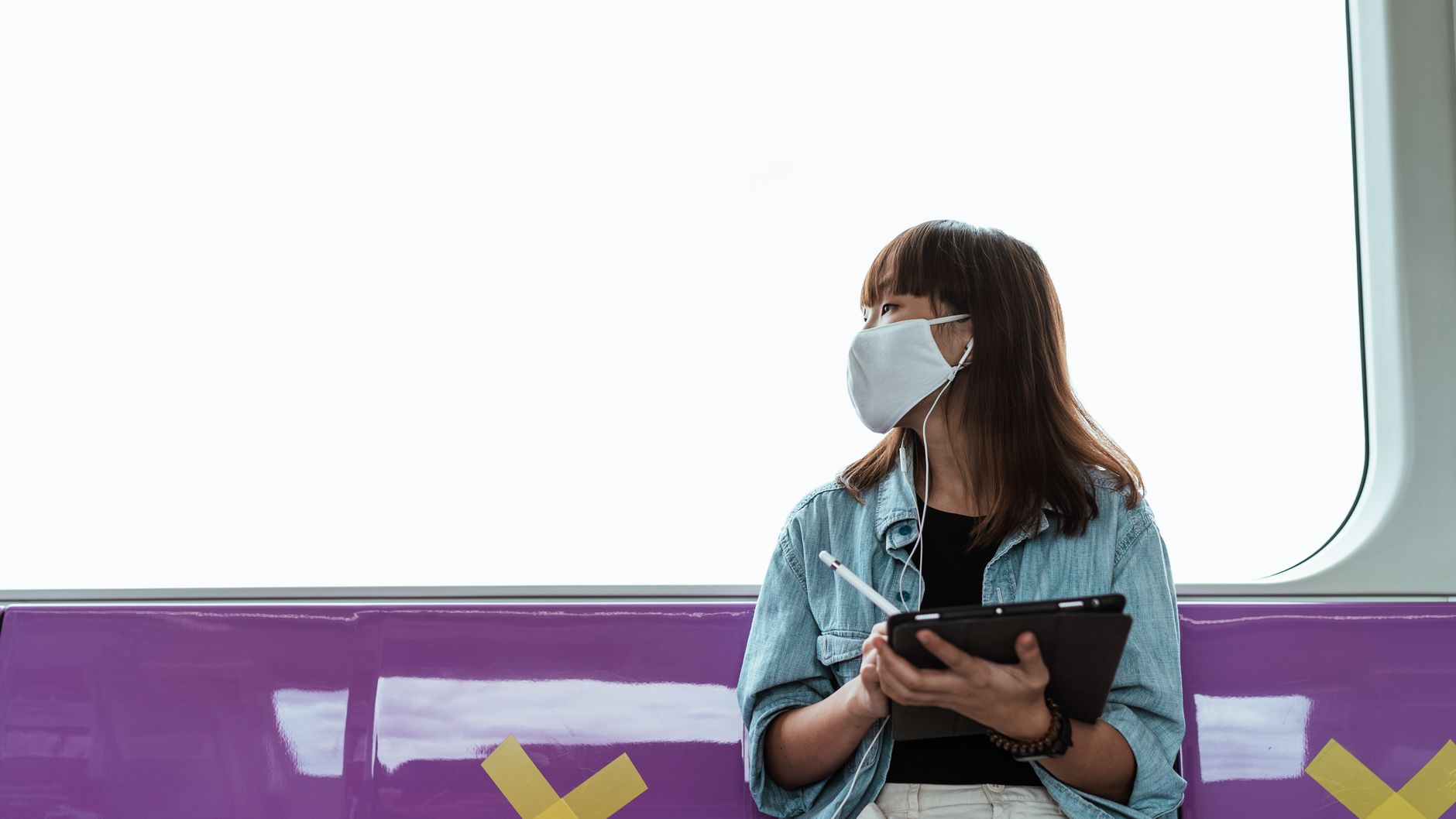 Woman wearing a face mask using a tablet on a train during the pandemic.