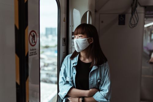 Free Asian woman in denim looking out subway window wearing a face mask during pandemic. Stock Photo