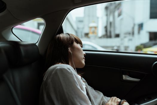 一名身穿白衬衫的冷漠女性在城市骑行途中，坐在汽车副驾驶座上休息，戴着耳机听音乐的侧面图