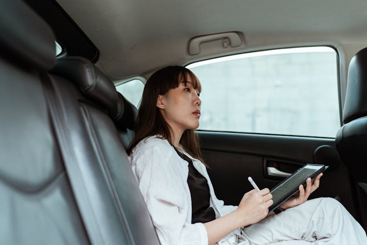 Focused Woman With Tablet And Stylus In Car Passenger Seat