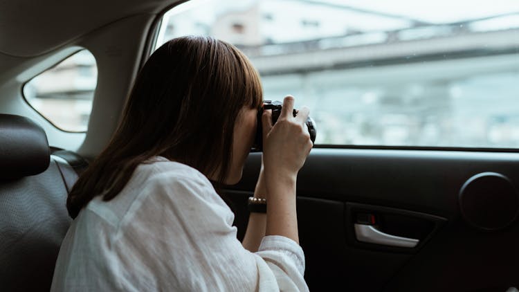 Woman Taking Photo On Photo Camera From Car Backseat
