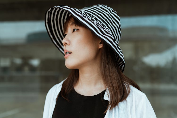 Content Asian Woman In Hat Against Glass Wall