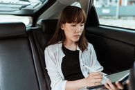 一名穿着休闲服装的亚洲女性，在有手写笔的现代平板电脑上工作，她正坐在汽车后座