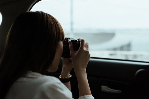 白天，一名穿着白衬衫的黑发女子坐在汽车乘客座位上，从后面拍摄城市建筑
