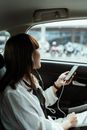 一位年轻女子坐在车里，用智能手机和耳机听着音乐