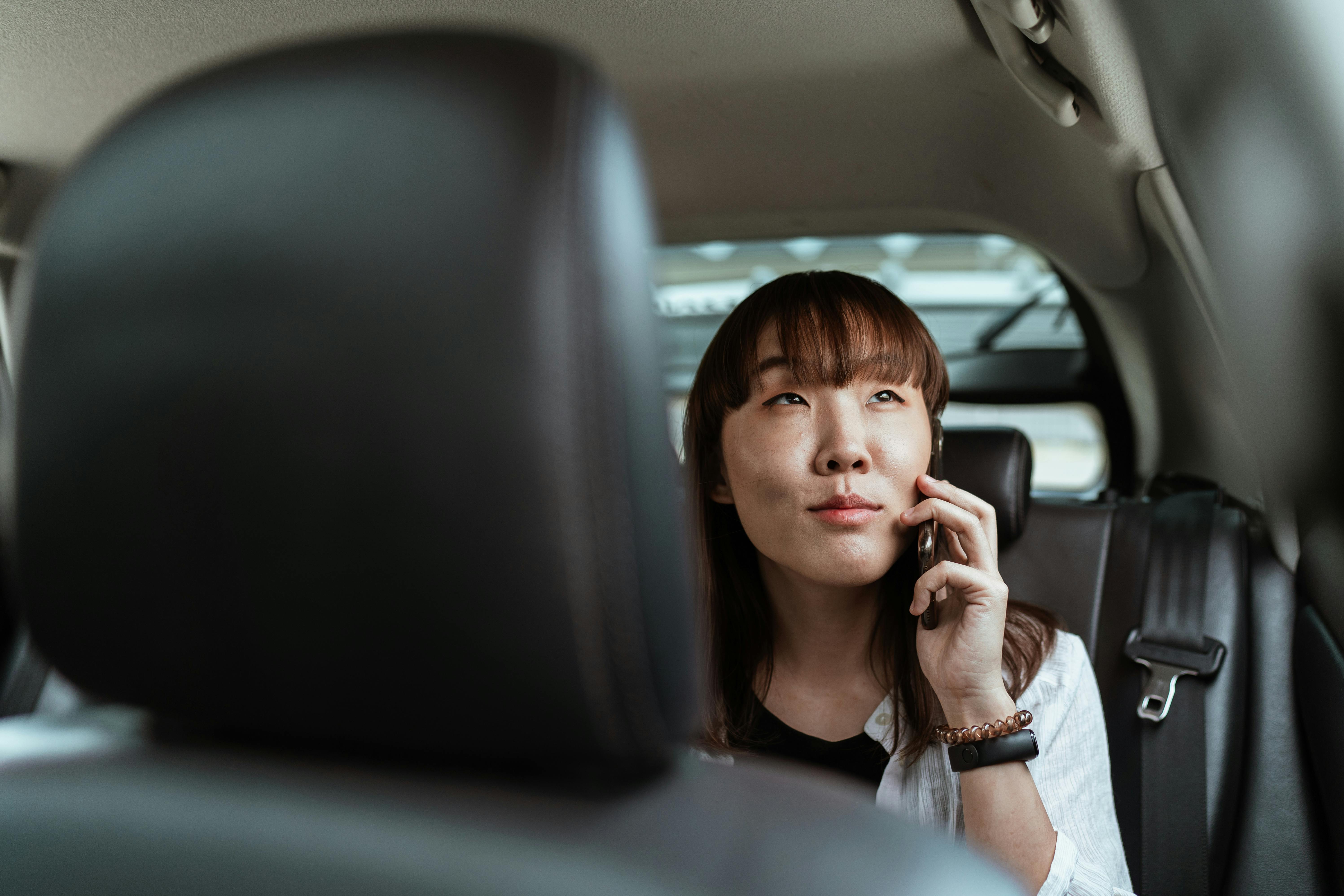 smiling asian lady talking on smartphone in car