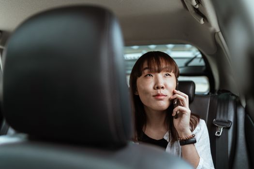 一名年轻女子坐在汽车后座上，正打着电话