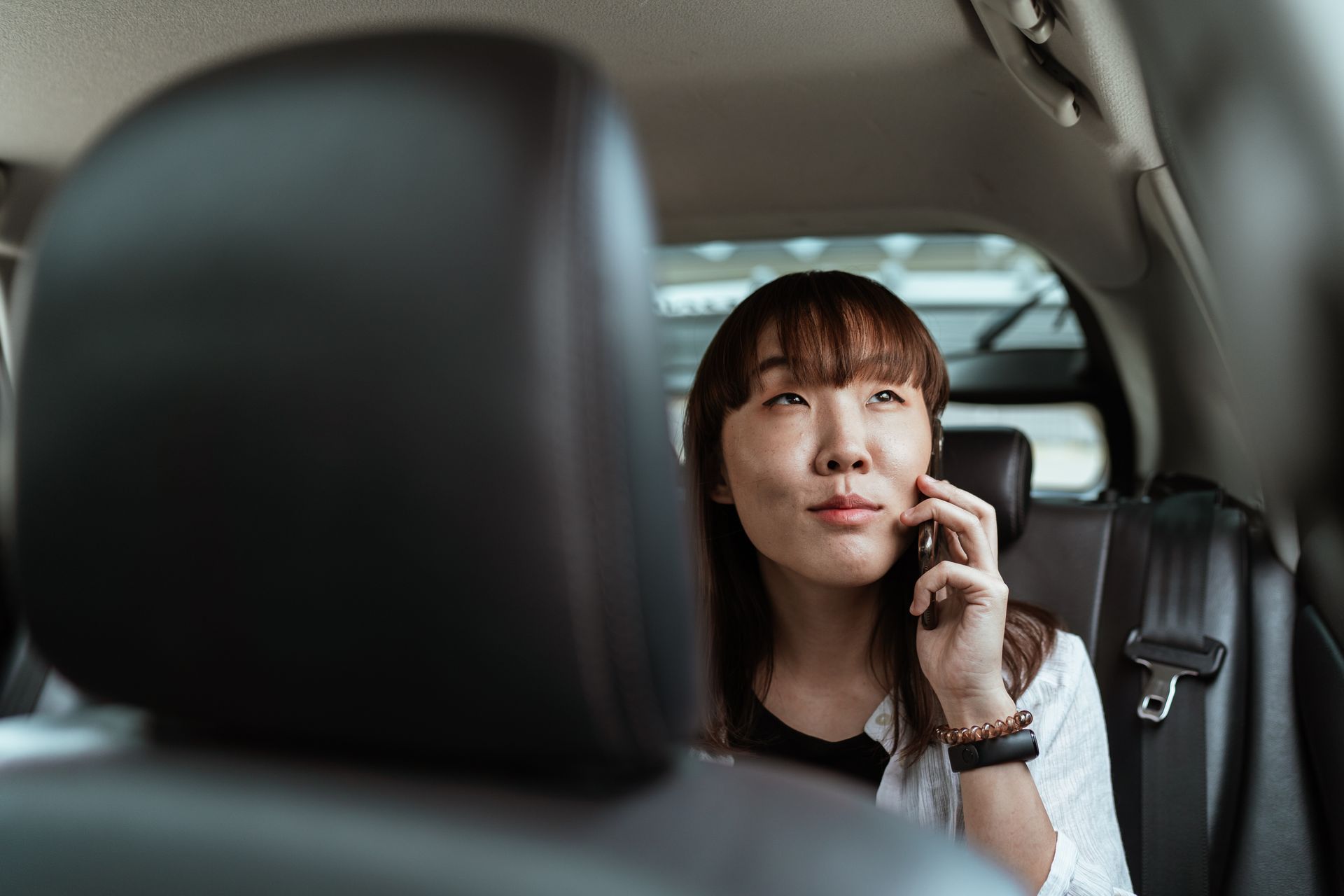 A young woman enjoys a phone conversation while sitting in a car's backseat.
