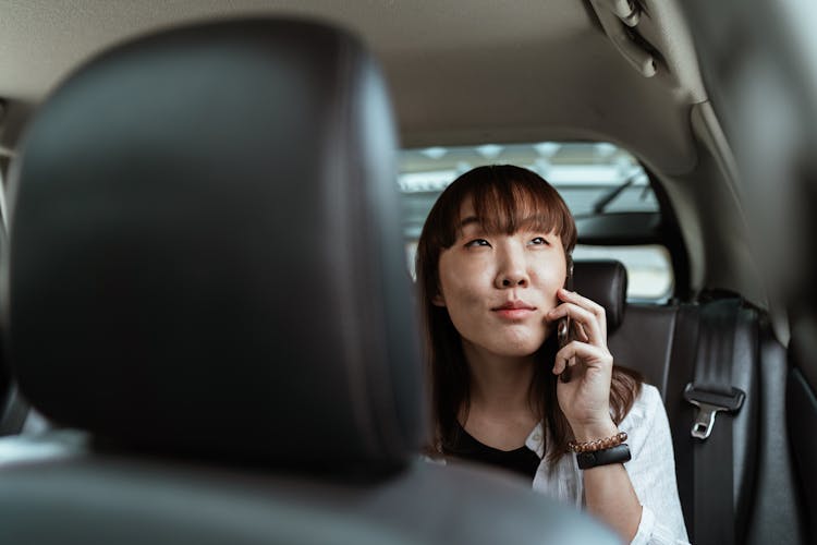 Smiling Asian Lady Talking On Smartphone In Car