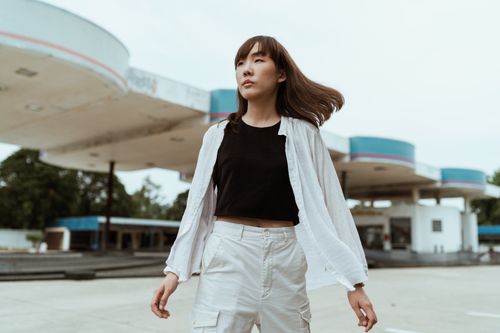 Free Serious young Asian female in black top with stylish white trousers and shirt standing on street and looking away thoughtfully Stock Photo