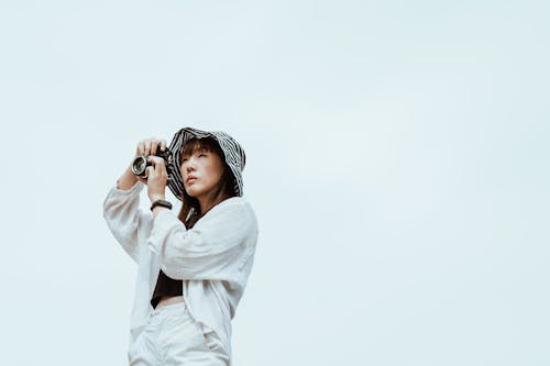 Pensive Asian model with photo camera on blue background