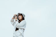 一位时尚女士戴着帽子，以晴朗的天空为背景，正在用相机拍摄