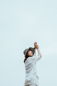 从后面看去，一位身着休闲装的梦幻亚洲女人正站在蓝墙附近，双手举起，抬头仰望
